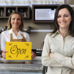two ladies in business holding an open sign
